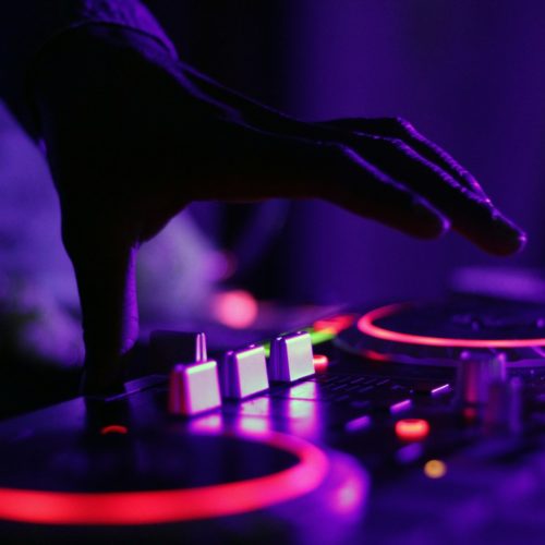 selective focus silhouette photography of man playing red-lighted DJ terminal